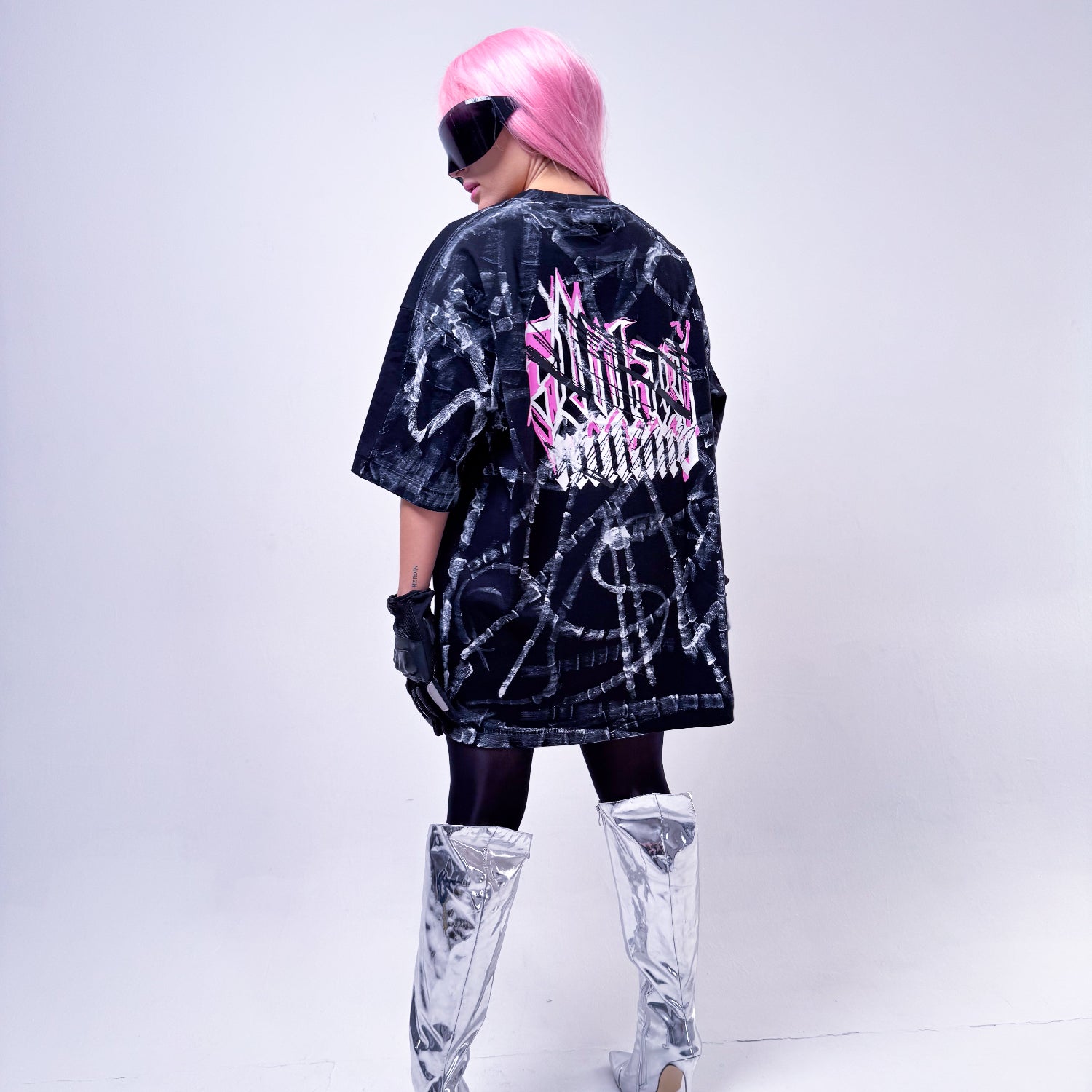 Person wearing a black tie-dye shirt with pink text and white knee-high boots on a white background